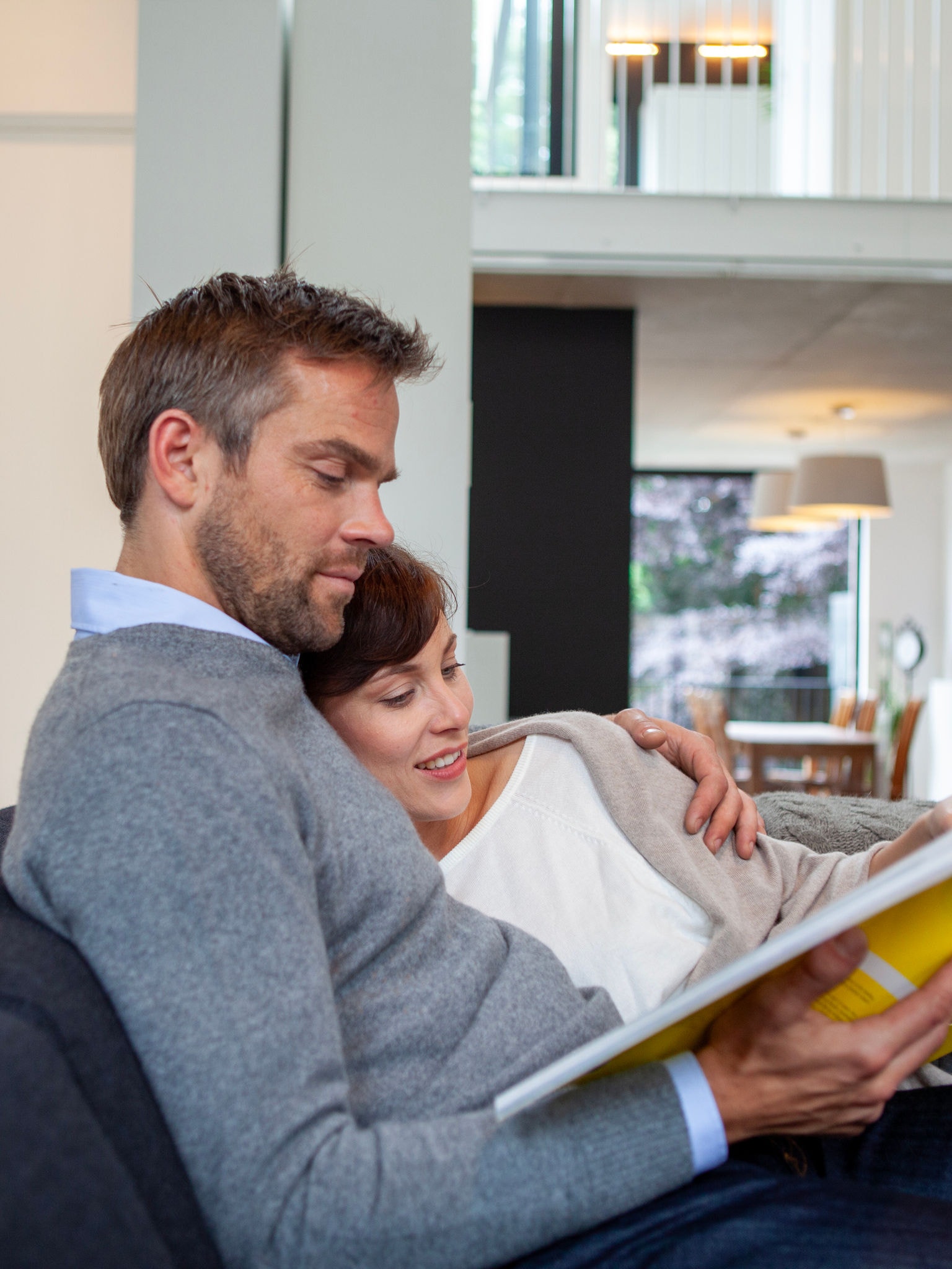 Ζευγάρι που χαλαρώνει αγκαλιασμένο στον καναπέ διαβάζοντας ένα βιβλίο, σε τέλεια θερμοκρασία