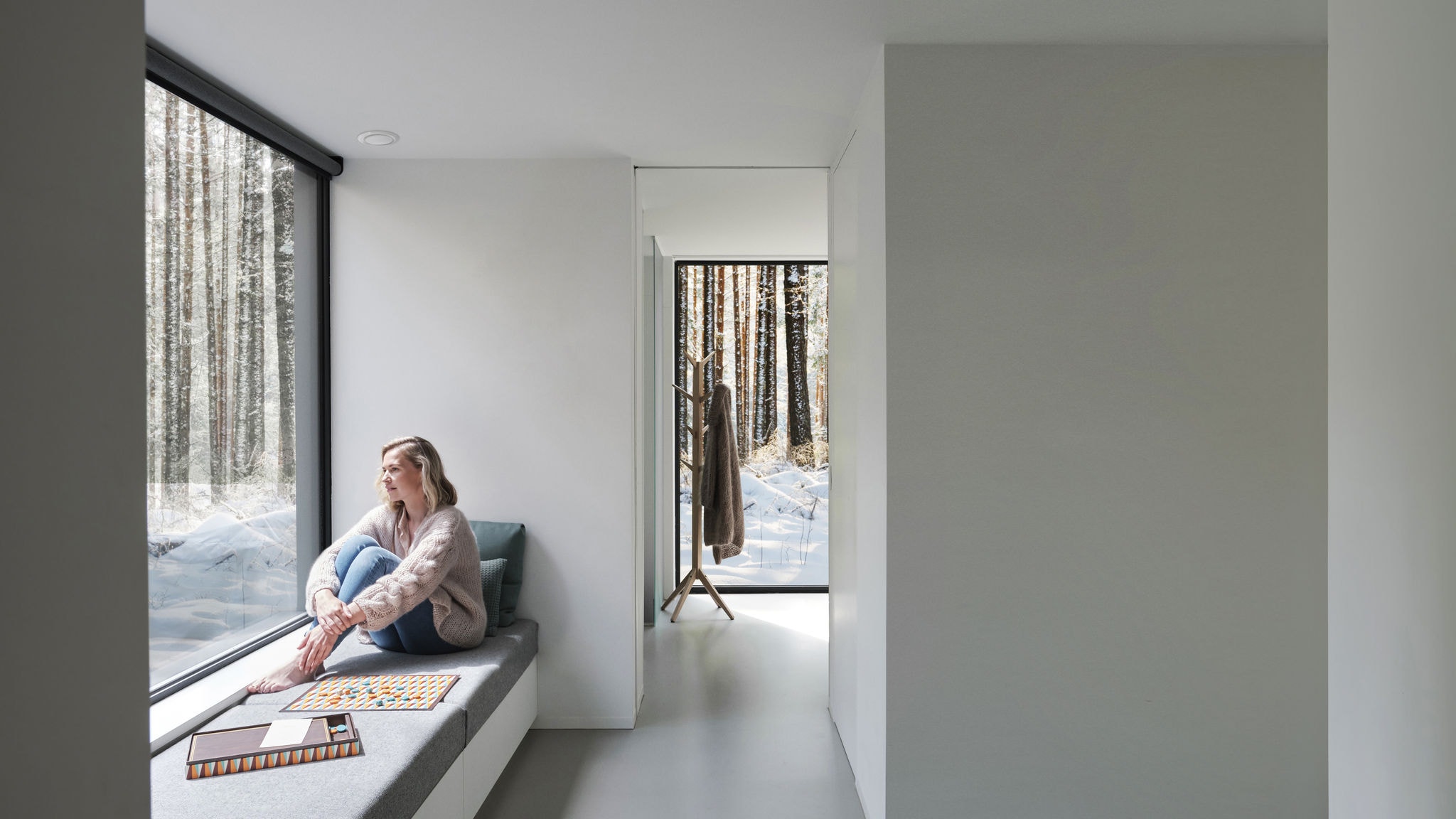Μακρινό πλάνο μιας γυναίκας που κάθεται μπροστά από ένα παράθυρο ξυπόλητη, κοιτάζοντας έξω τα δέντρα και το χιόνι.