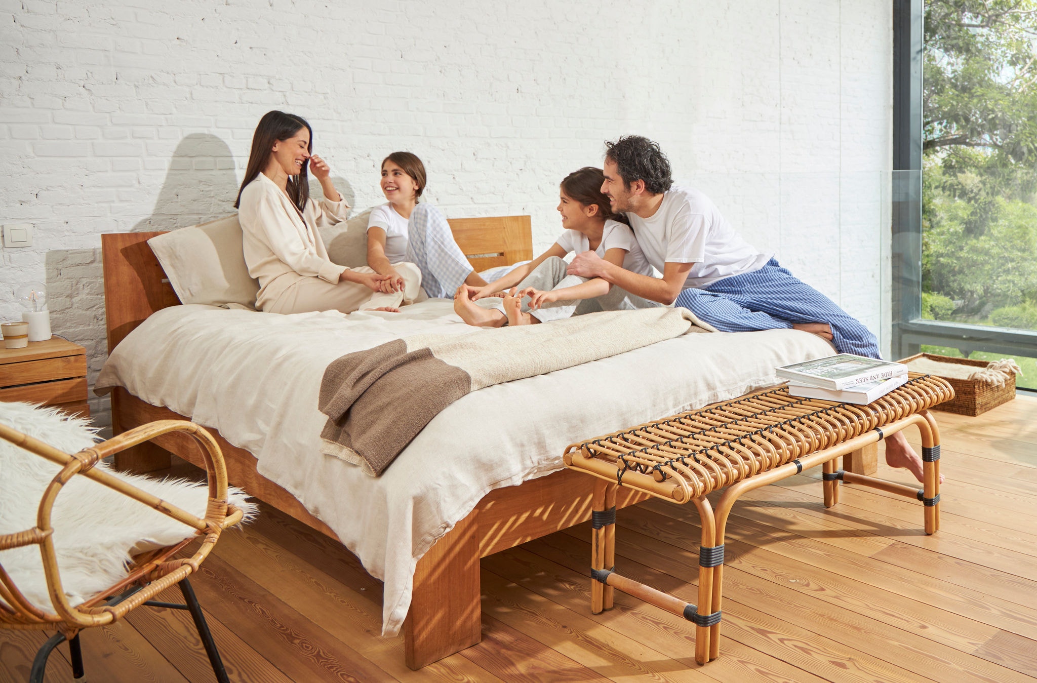 Μια γυναίκα και ένας άντρας κάθονται σε ένα κρεβάτι με δύο νεαρά κορίτσια, χαλαρώνοντας, γελώντας και απολαμβάνοντας υγιεινό αέρα.