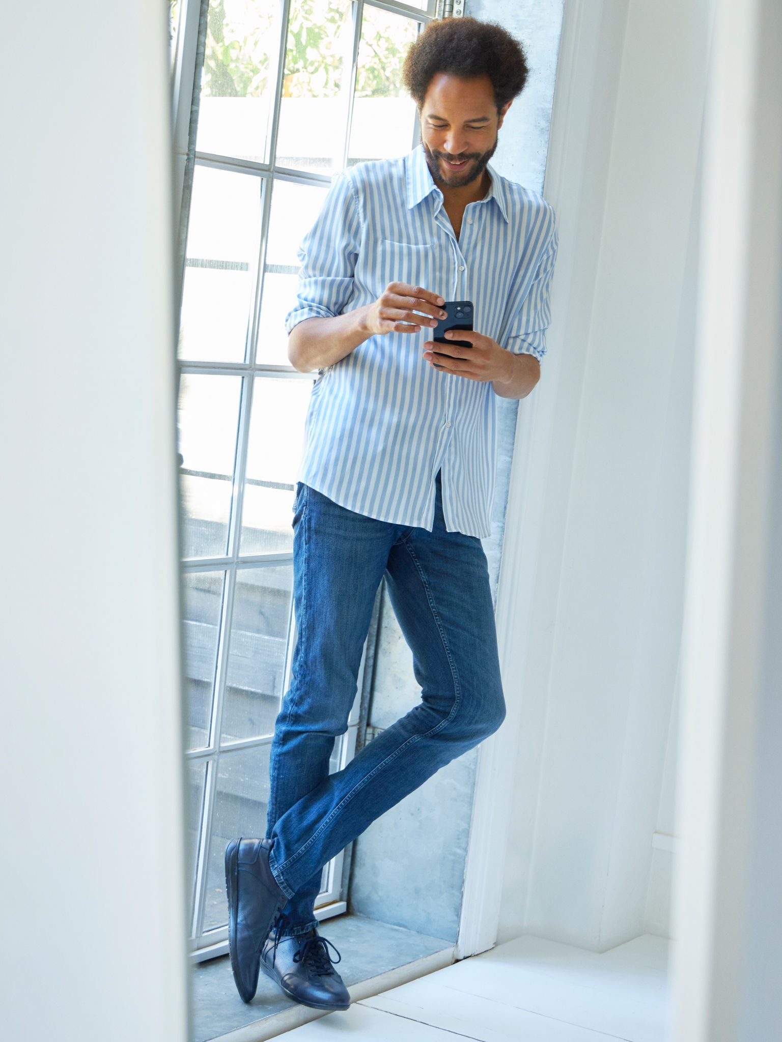 Άντρας που στέκεται κοντά σε ένα παράθυρο βλέποντας κλιματιστικά στο εικονικό κέντρο εμπειρίας στο smartphone του