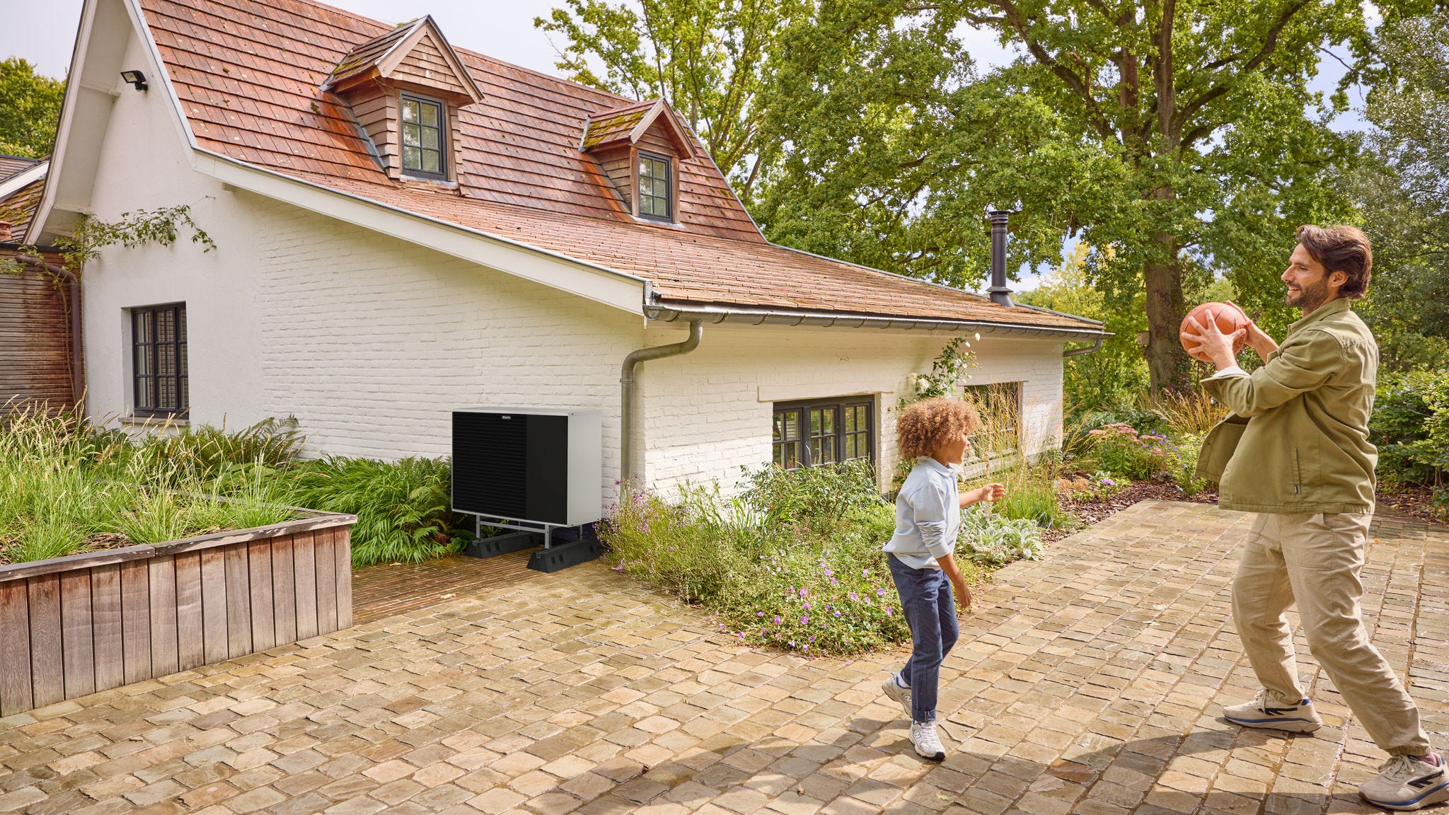 Πατέρας παίζει με το παιδί του έξω σε έναν κήπο, με μια αντλία θερμότητας εγκατεστημένη κοντά