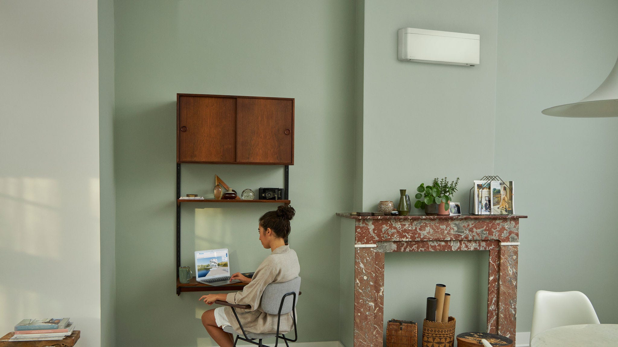 Γυναίκα που επισκέπτεται το Εικονικό Κέντρο Εμπειρίας της Daikin μέσω του φορητού υπολογιστή της, από το μικρό γραφείο της σε ένα όμορφα διακοσμημένο καθιστικό