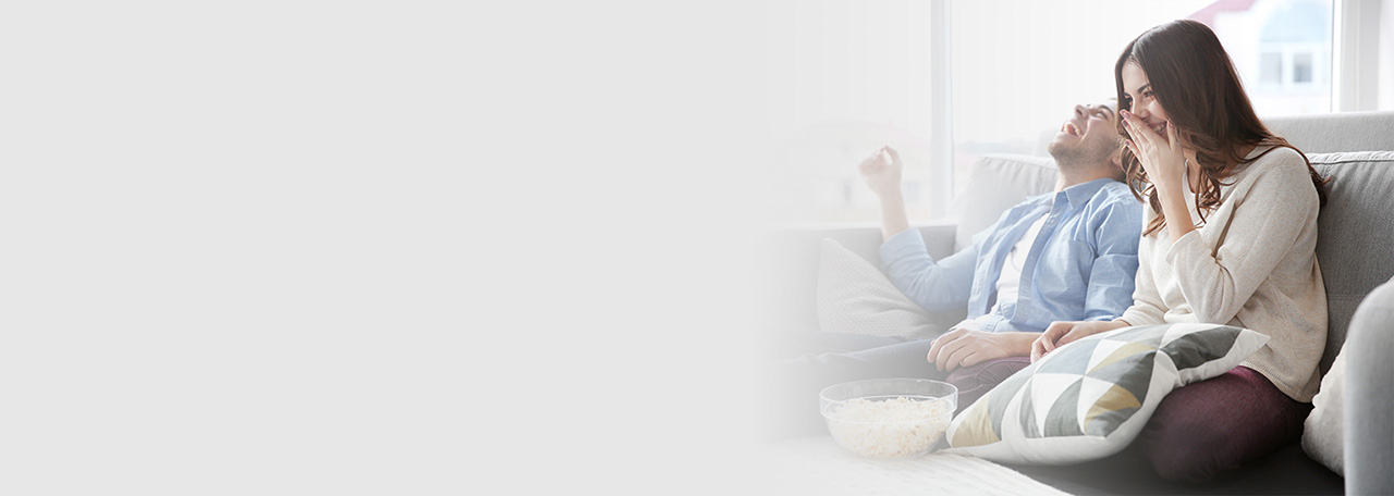 Ζευγάρι που γελάει ενώ κάθεται σε καναπέ τρώγοντας ποπ-κορν.